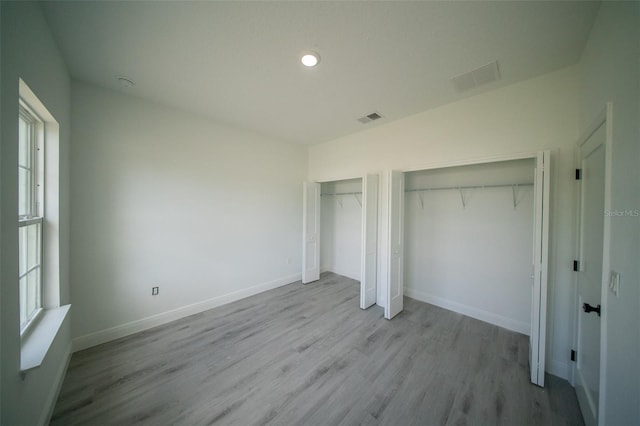unfurnished bedroom featuring baseboards, visible vents, two closets, and wood finished floors