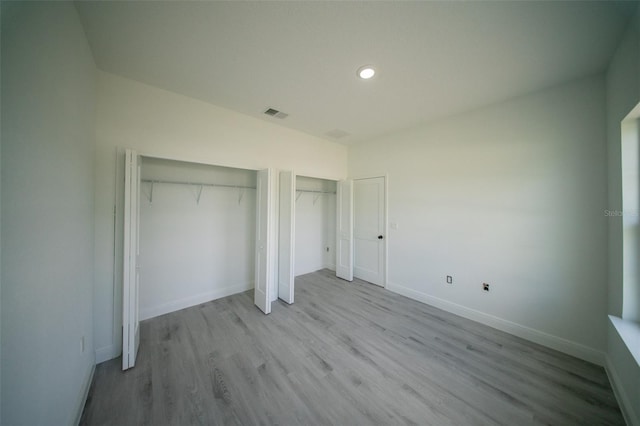unfurnished bedroom with wood finished floors, multiple closets, visible vents, baseboards, and recessed lighting