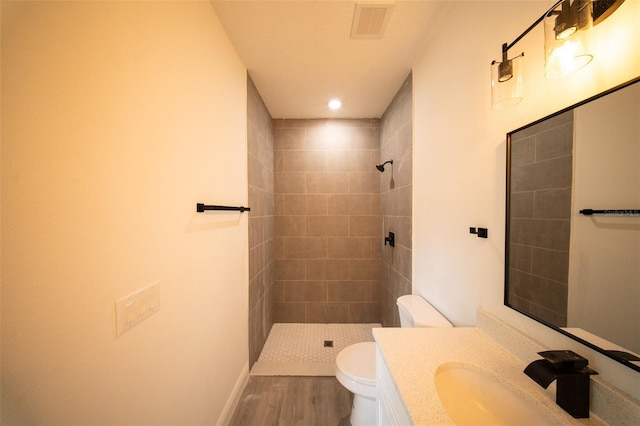 bathroom featuring vanity, a tile shower, toilet, and wood finished floors