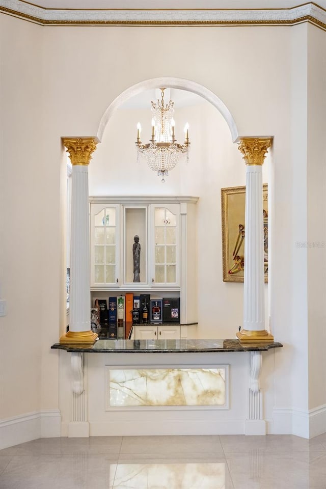 indoor bar featuring arched walkways, decorative columns, a chandelier, tile patterned floors, and baseboards