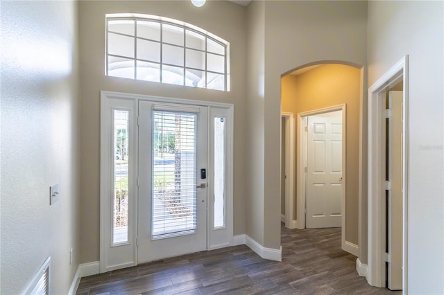 foyer entrance with visible vents, baseboards, arched walkways, and dark wood-style floors