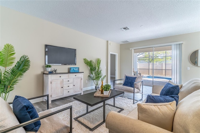 living room featuring a textured ceiling, visible vents, wood finished floors, and baseboards