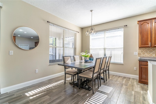 dining space with a textured ceiling, wood finished floors, baseboards, and a notable chandelier