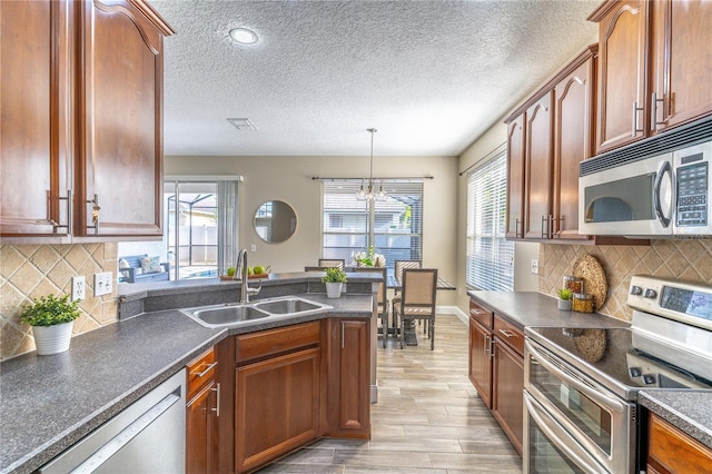 kitchen featuring a sink, dark countertops, a healthy amount of sunlight, light wood-type flooring, and appliances with stainless steel finishes