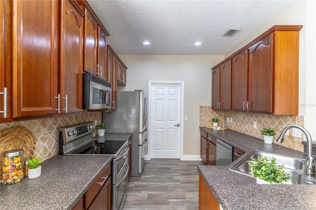 kitchen featuring a textured ceiling, a sink, dark countertops, appliances with stainless steel finishes, and dark wood-style floors