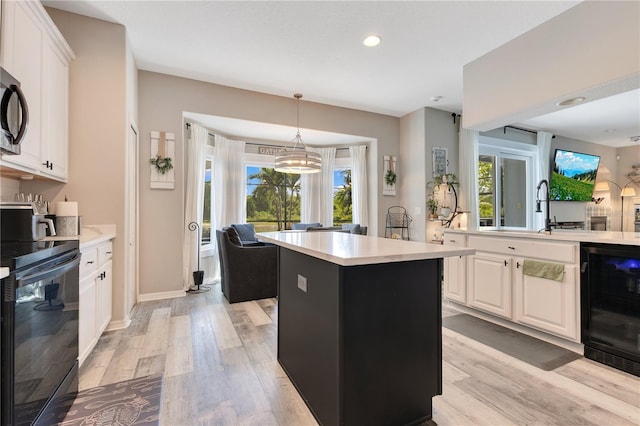 kitchen featuring beverage cooler, light countertops, black electric range, and light wood-type flooring