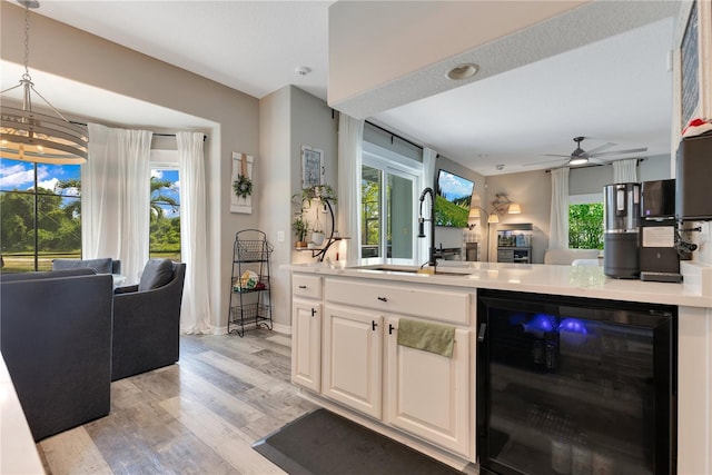 bar with light wood-style flooring, a ceiling fan, a sink, baseboards, and wine cooler