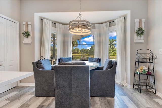 dining space with light wood-style flooring, a notable chandelier, and baseboards
