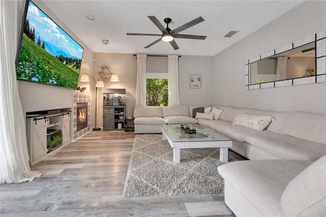 living area with light wood finished floors, visible vents, a fireplace, and ceiling fan