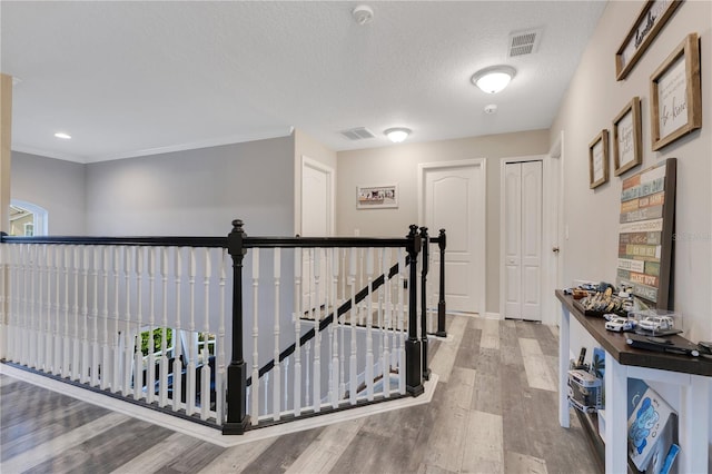 hallway featuring a textured ceiling, visible vents, an upstairs landing, and wood finished floors
