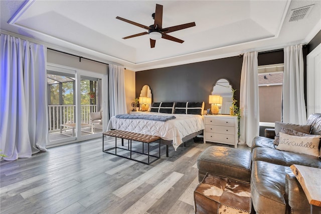 bedroom featuring wood finished floors, access to exterior, a ceiling fan, visible vents, and a raised ceiling