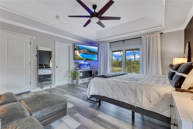 bedroom featuring wood finished floors, ornamental molding, a ceiling fan, a tray ceiling, and access to outside