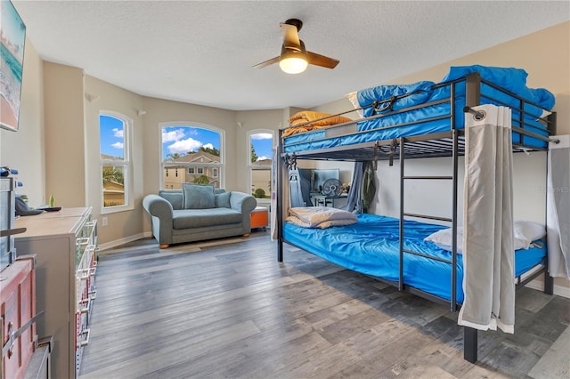 bedroom featuring baseboards, ceiling fan, a textured ceiling, and wood finished floors