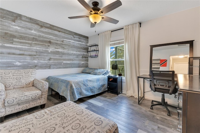 bedroom featuring an accent wall, ceiling fan, wooden walls, and wood finished floors