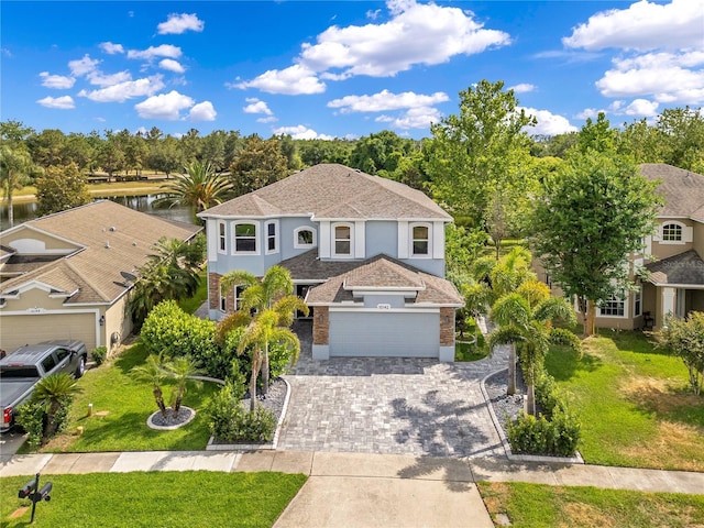traditional home with a water view, a garage, stucco siding, a front lawn, and decorative driveway