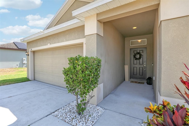 view of exterior entry with stucco siding, driveway, and an attached garage