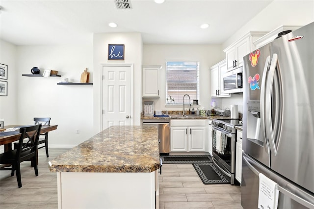 kitchen featuring stainless steel appliances, a sink, white cabinetry, wood finish floors, and recessed lighting