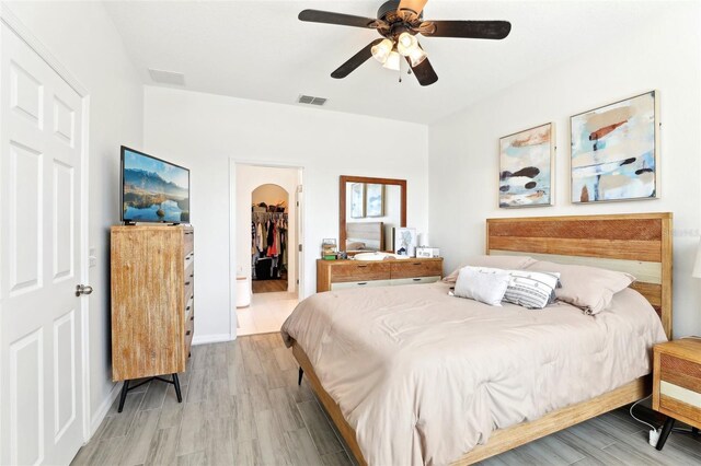 bedroom with a walk in closet, light wood-type flooring, arched walkways, a closet, and a ceiling fan