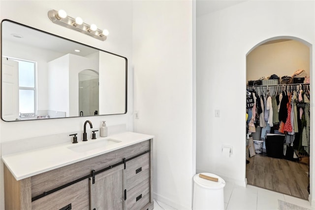 full bathroom featuring vanity, a walk in closet, baseboards, and tile patterned floors