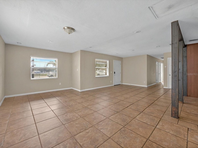 unfurnished room with light tile patterned floors, healthy amount of natural light, baseboards, and a textured ceiling