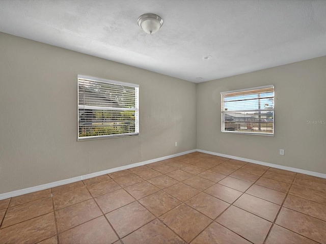 tiled empty room with a textured ceiling and baseboards
