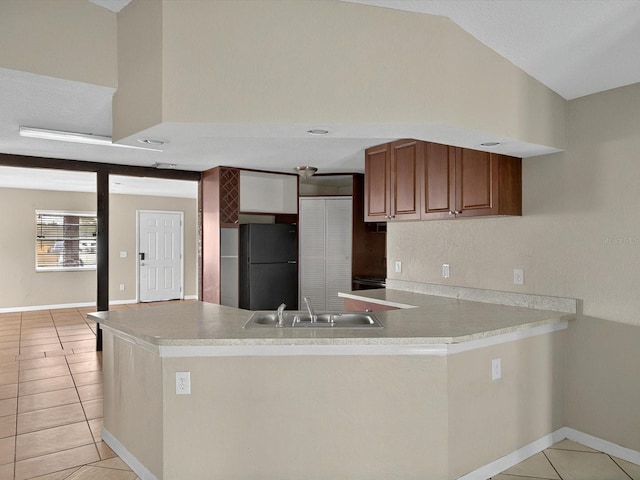 kitchen featuring freestanding refrigerator, a sink, light tile patterned floors, a peninsula, and light countertops