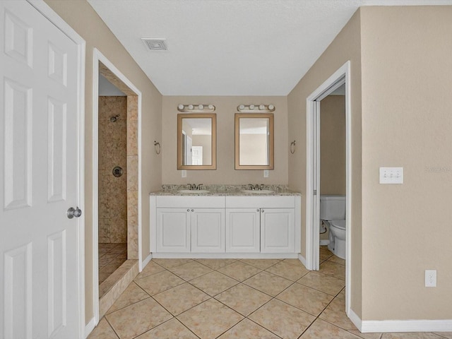 full bathroom with a tile shower, tile patterned flooring, toilet, double vanity, and baseboards