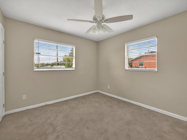 carpeted empty room with healthy amount of natural light, a ceiling fan, baseboards, and a textured ceiling