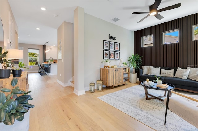 living area with baseboards, light wood finished floors, ceiling fan, visible vents, and an accent wall