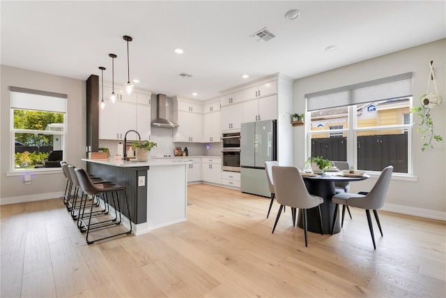 kitchen with a peninsula, freestanding refrigerator, visible vents, white cabinetry, and baseboards