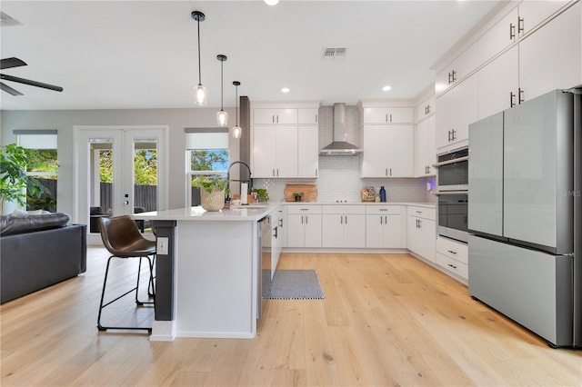 kitchen with a peninsula, a ceiling fan, visible vents, wall chimney range hood, and appliances with stainless steel finishes