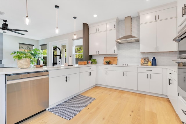 kitchen featuring light countertops, wall chimney exhaust hood, stainless steel dishwasher, and backsplash