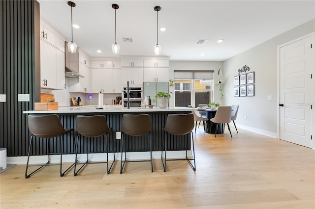 kitchen featuring a peninsula, freestanding refrigerator, a breakfast bar area, visible vents, and light countertops