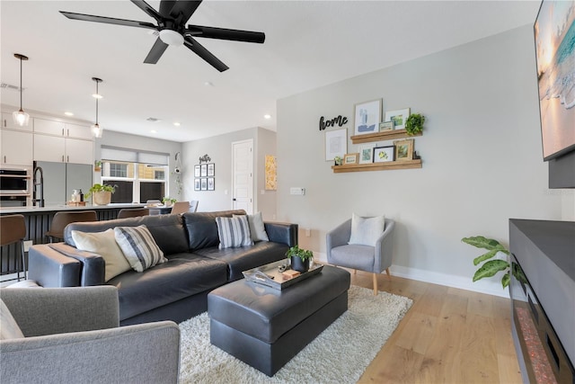 living area featuring baseboards, light wood-style flooring, a ceiling fan, and recessed lighting