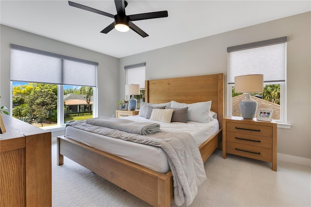 bedroom featuring ceiling fan, light carpet, baseboards, and multiple windows
