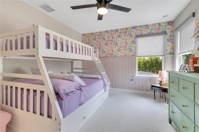bedroom with carpet flooring, wallpapered walls, visible vents, wainscoting, and ceiling fan