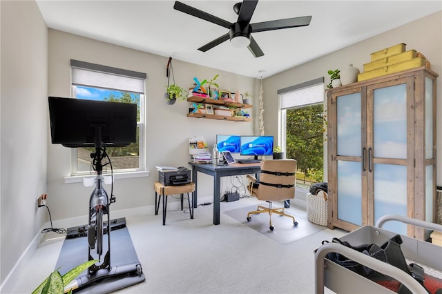 carpeted office space with ceiling fan and baseboards