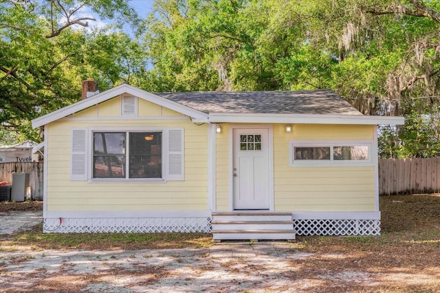 bungalow-style house with roof with shingles, a chimney, fence, and entry steps