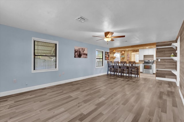 living area with light wood-style floors, visible vents, baseboards, and ceiling fan