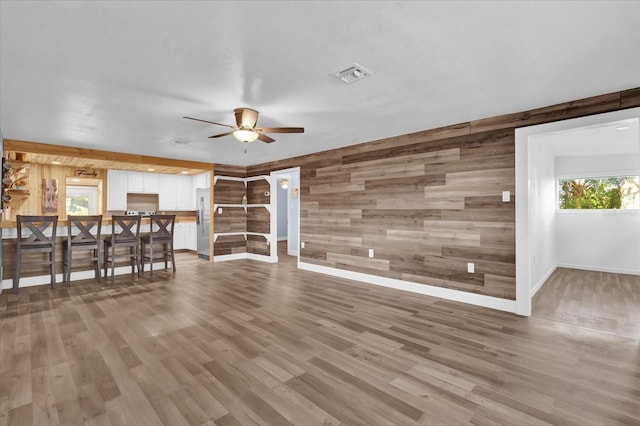 unfurnished living room with wooden walls, baseboards, a ceiling fan, and visible vents