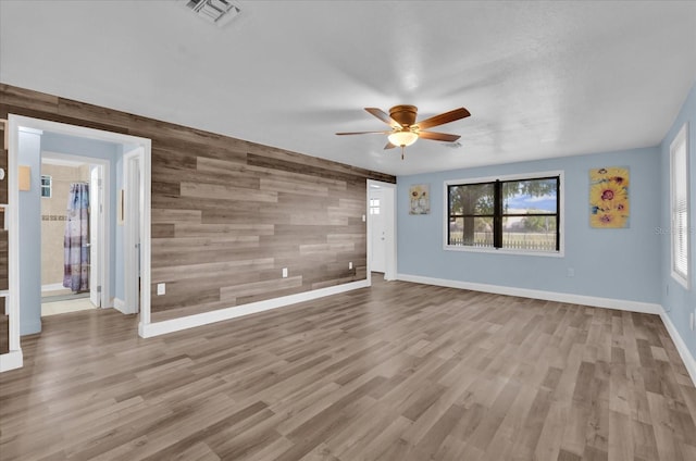 unfurnished living room featuring wood finished floors, a ceiling fan, visible vents, an accent wall, and wooden walls