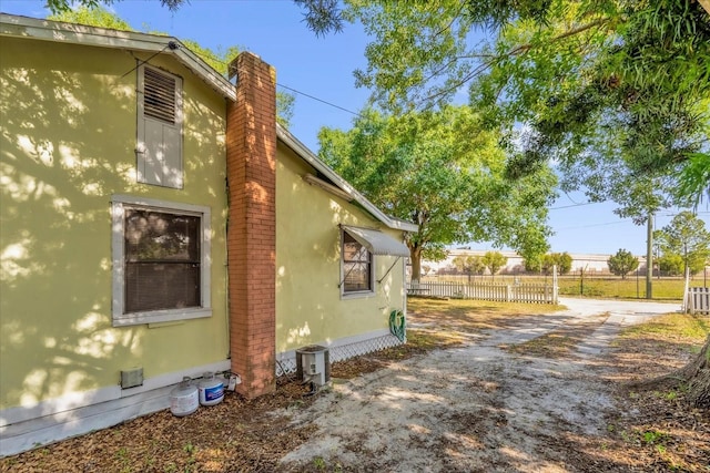 view of property exterior with dirt driveway, stucco siding, a chimney, and fence