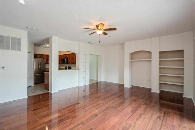 unfurnished living room featuring ceiling fan, arched walkways, visible vents, and wood finished floors