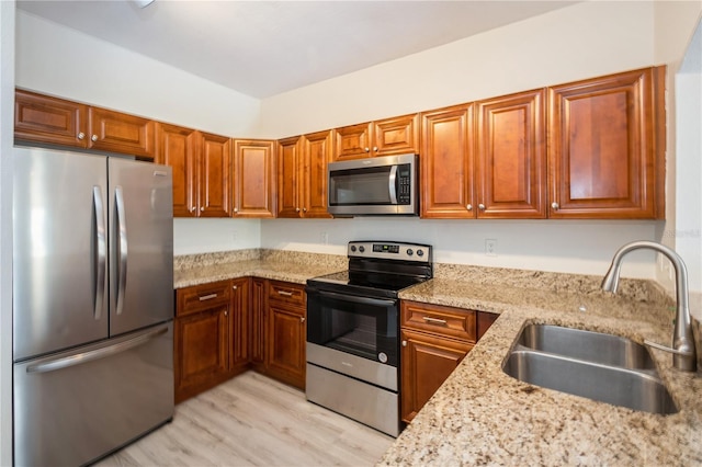 kitchen featuring light stone counters, light wood finished floors, a sink, brown cabinets, and appliances with stainless steel finishes