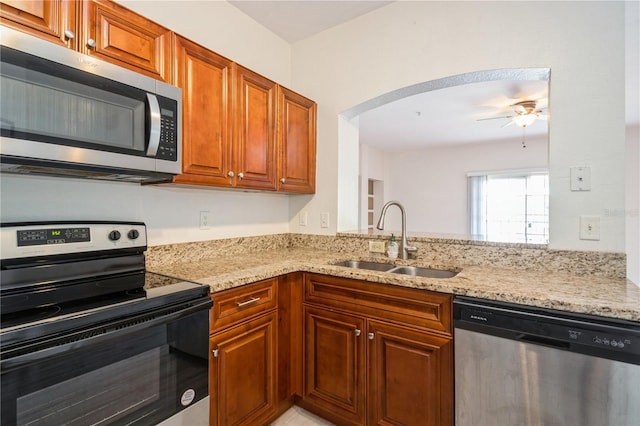 kitchen with a ceiling fan, light stone counters, stainless steel appliances, and a sink