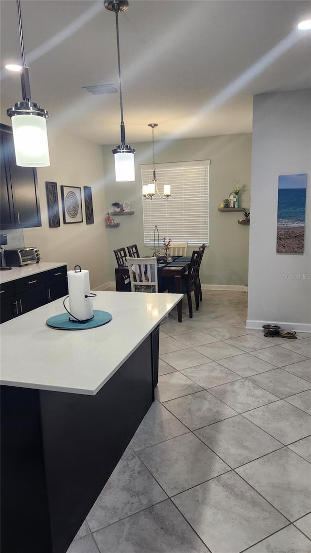 kitchen with light countertops, light tile patterned floors, dark cabinets, hanging light fixtures, and baseboards