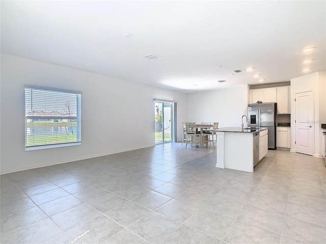 kitchen featuring dark countertops, light tile patterned floors, open floor plan, a center island with sink, and white cabinetry