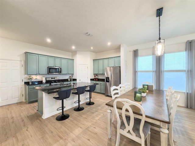kitchen with appliances with stainless steel finishes, dark countertops, a kitchen bar, light wood-style floors, and a sink