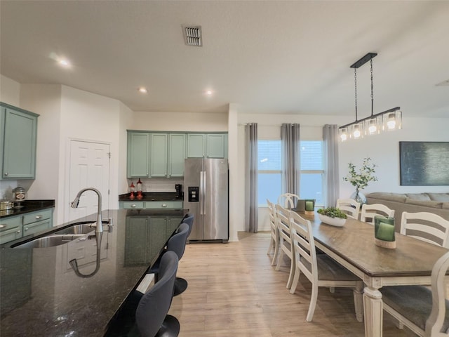 kitchen with stainless steel refrigerator with ice dispenser, a sink, green cabinetry, light wood finished floors, and recessed lighting