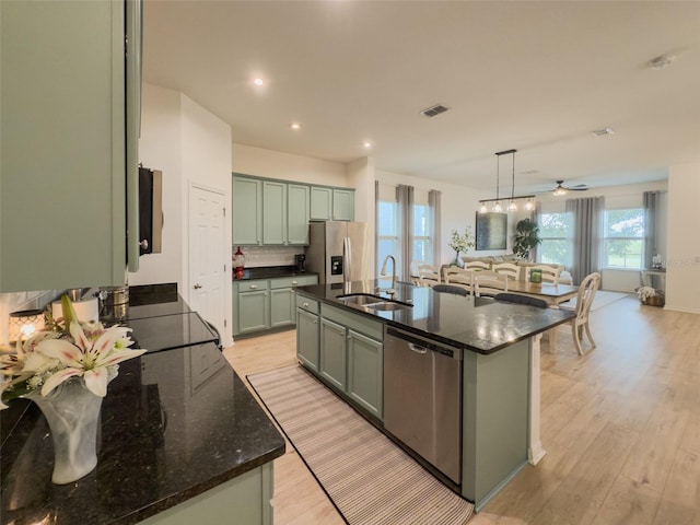 kitchen with a sink, appliances with stainless steel finishes, light wood finished floors, green cabinetry, and a center island with sink